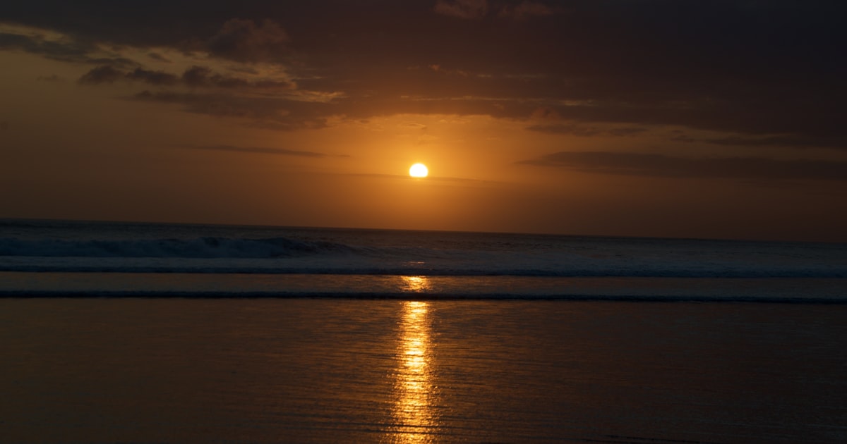 The sun is setting over the ocean on a cloudy day