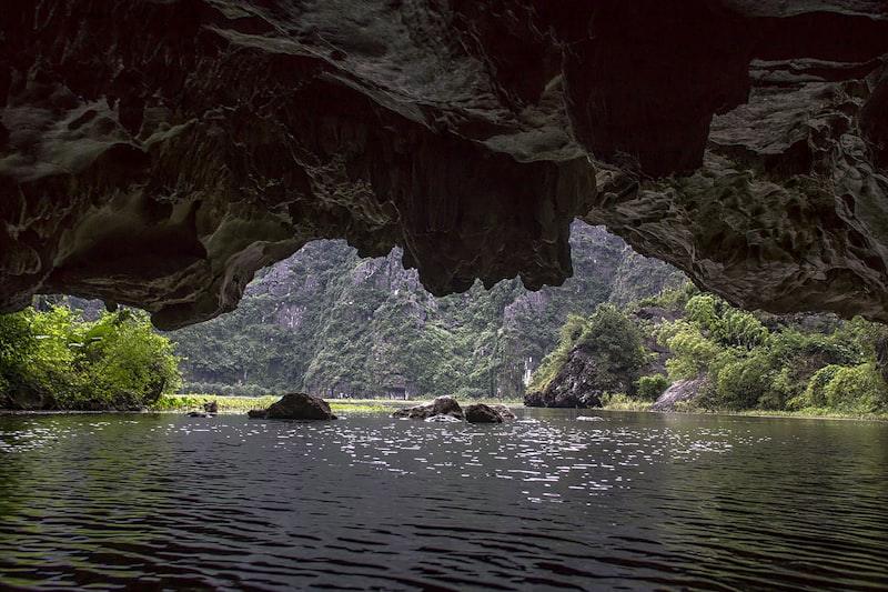A river flows through a cave towards lush green mountains.