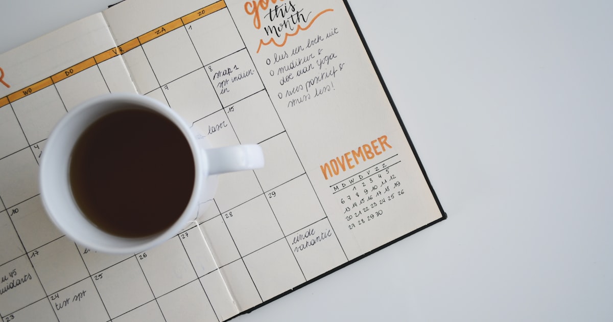 white ceramic mug with coffee on top of a planner