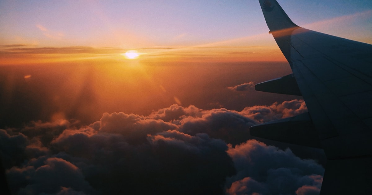Airplane flying over clouds at sunset with orange sky
